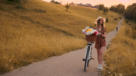 Slow-motion-sexy-beautiful-woman-with-a-bike-in-a-hat-and-a-light-summer-dress-comes-with-flowers-in-a-basket-and-smiles.